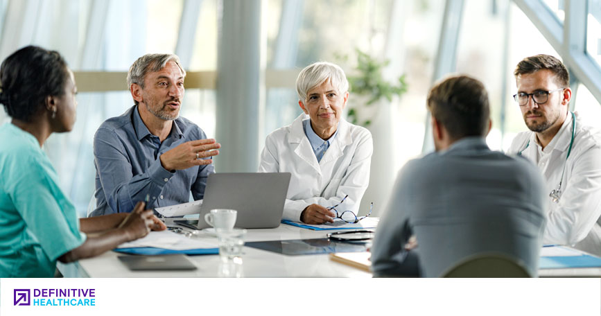 A group of clinicians sits around a table and talks.