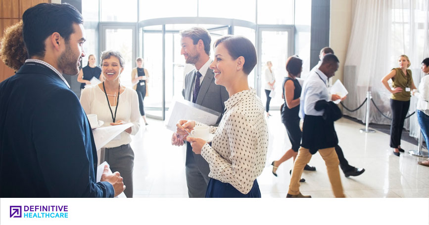 A group of men and woman in business outfits standing talking to each other in a foyer of a building