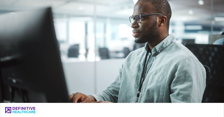 A healthcare professional sits at a desk and types on a computer.