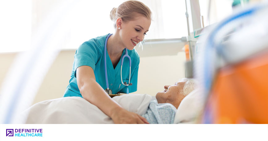 A nurse smiles as she tucks a patient into bed.