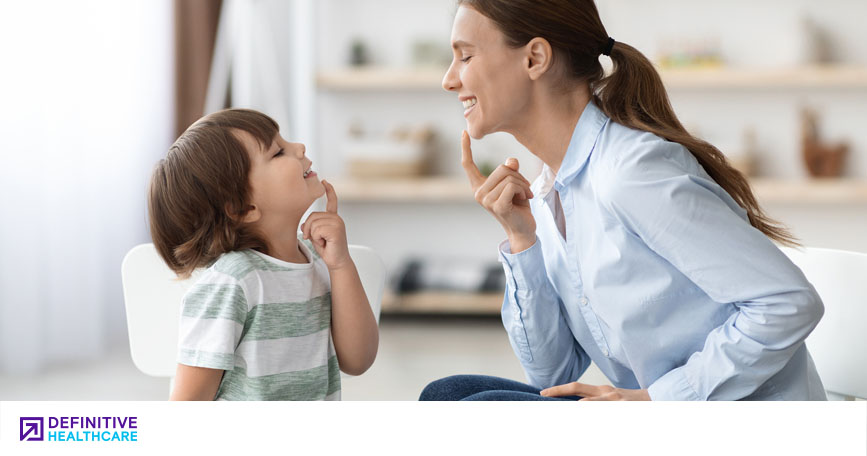 A woman leads a young child in a speech therapy exercise.
