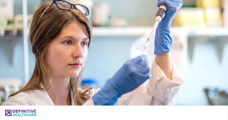 A researcher wearing a lab coat and blue gloves inserts an instrument into a vial.