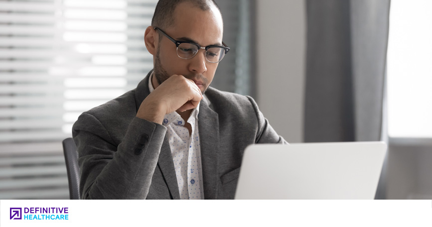 A man in professional attire looks down at his laptop screen.
