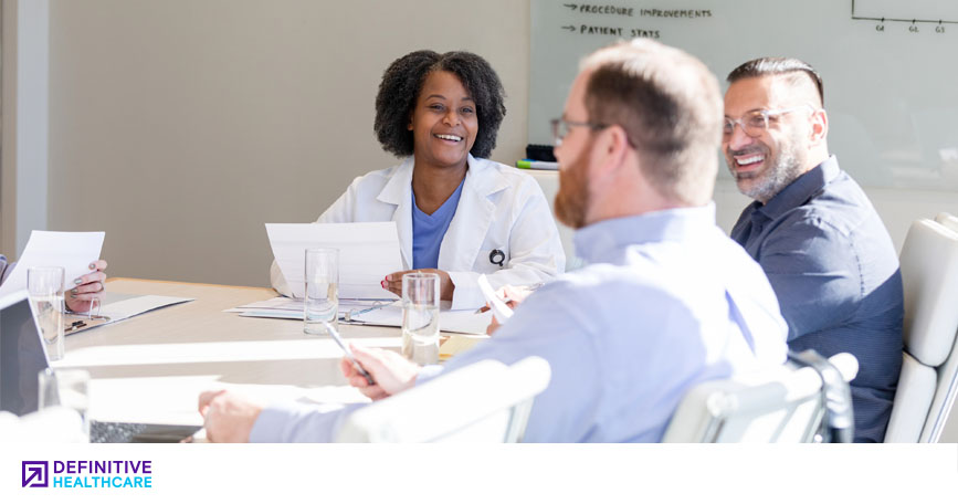A group of healthcare professionals sits around a conference table, looking at notes and smiling. 