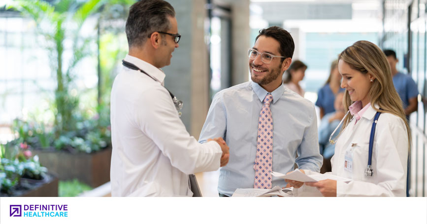 A medical science liaison smiles as he interacts with two healthcare professionals in a medical facility hallway.