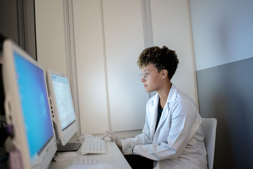 A female researcher sits at a desk and studies a computer monitor.