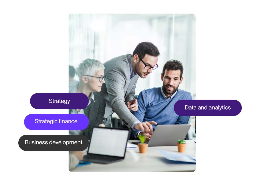 Three people in business attire look at a laptop. Two are sitting, one stands in the middle pointing at the screen.