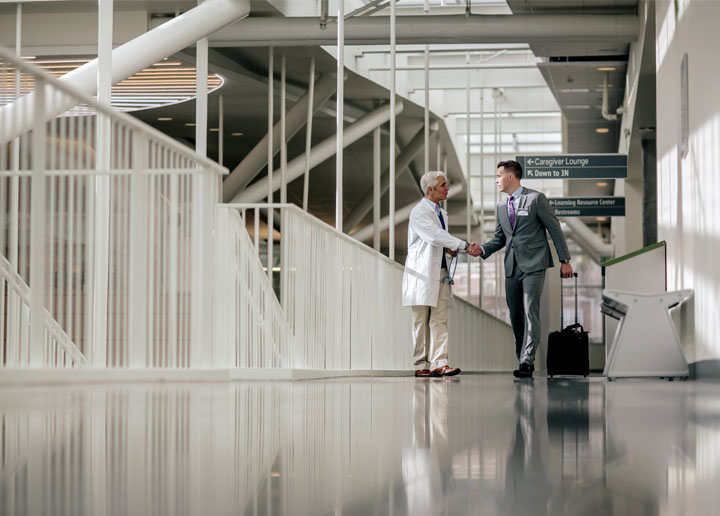 A male healthcare professional in a white coat shakes hands with a male dressed in business attire.