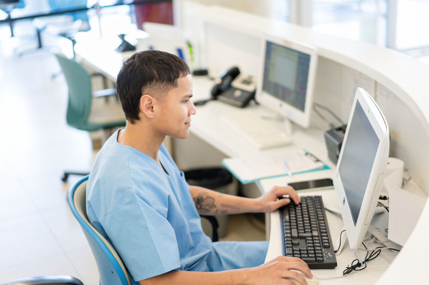 A healthcare professional sits at a desk while working on a computer.