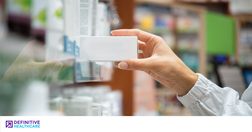 A close-up shot of a person's hand grabbing a box from a shelf in a pharmacy.