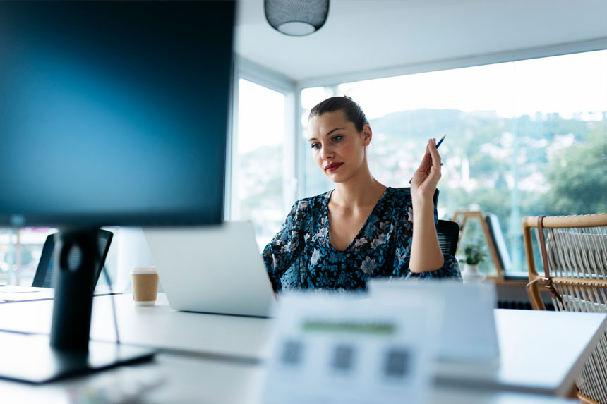 A healthcare marketing professional sits at a desk in a well-lit office and looks at her laptop. 