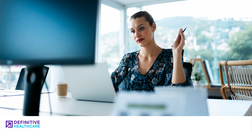 A healthcare marketing professional sits at a desk in a well-lit office and looks at her laptop.