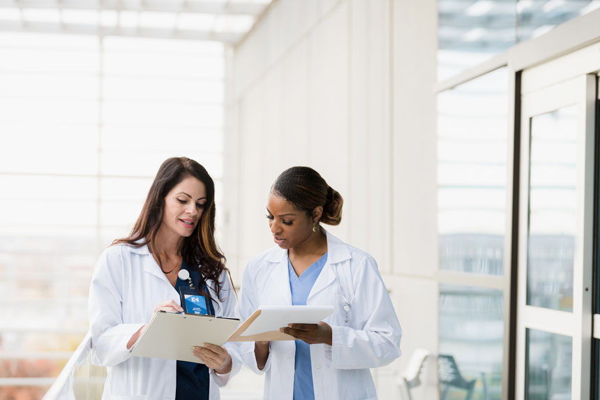 Two female healthcare professionals stand in a well-lit room and compare charts. 