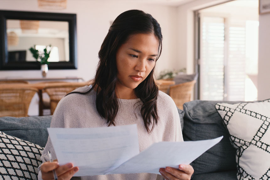 A female sits on a couch while holding up a piece of paper in each hand to read.