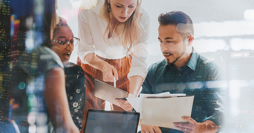 Marketing team members huddle over folders and a laptop to discuss strategy.