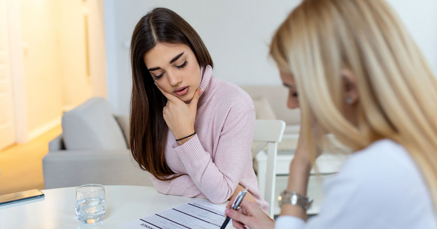 Two females sit at a table looking down at a paper.