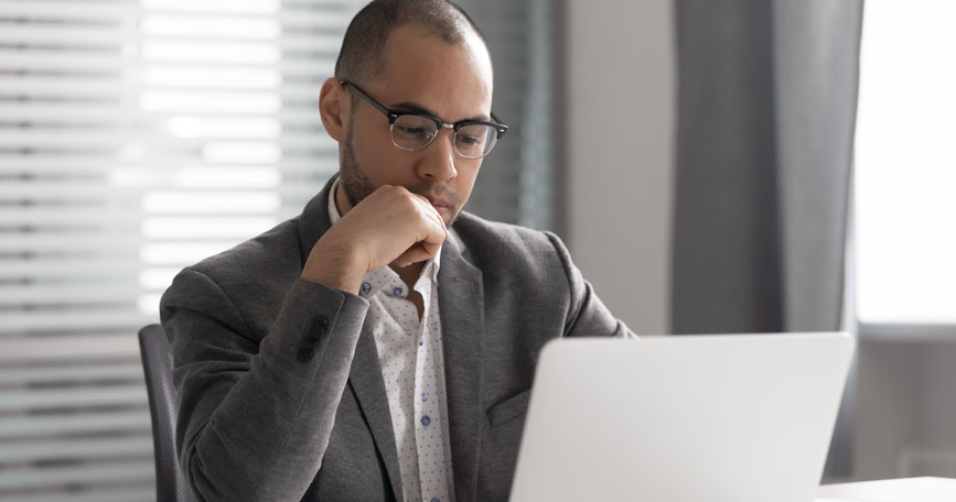 A man in professional attire looks down at his laptop screen.