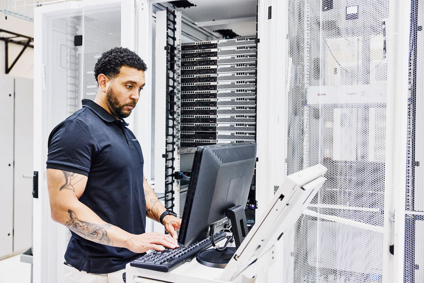 A cybersecurity professional stands at a computer workstation and types on a keyboard.