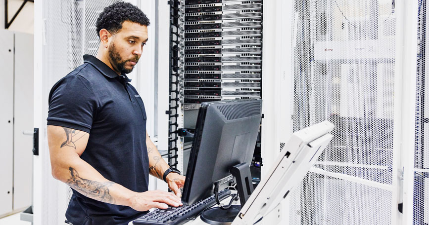 A cybersecurity professional stands at a computer workstation and types on a keyboard.