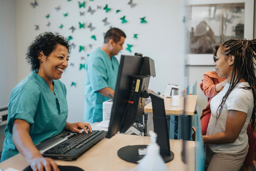 Smiling medical staff in light blue scrubs stand at a desk and assist patients in a rural clinic. 