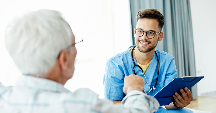 A healthcare professional smiles holding a clipboard while sitting across from a patient.