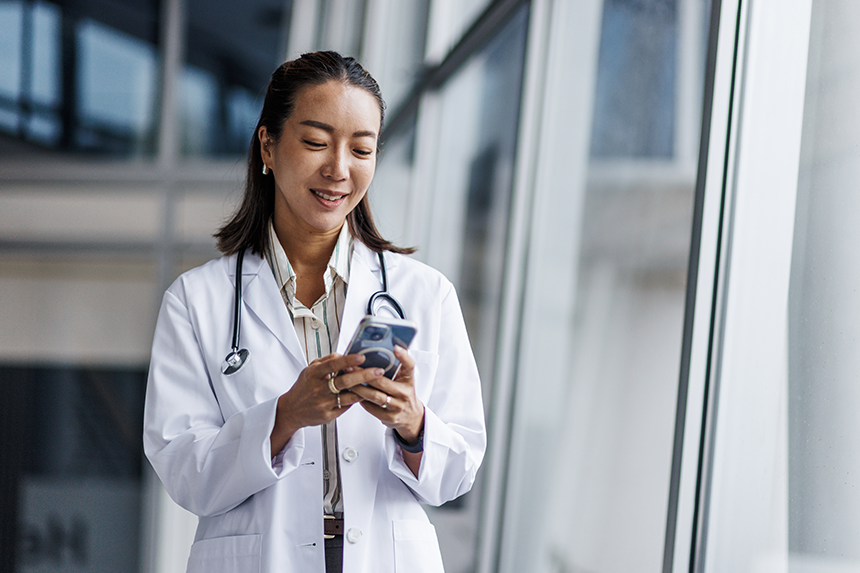 A female healthcare professional smiles while using her smartphone.