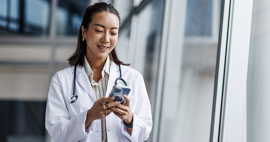 A female healthcare professional smiles while using her smartphone.