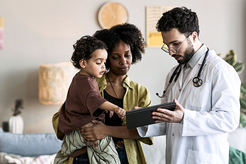 A physician reviews a chart with a woman while she holds her small child in her arms.
