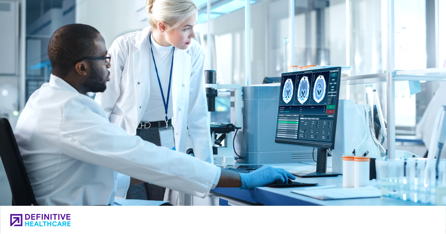 A Black male and a white woman in lab coats looking at a computer with medical images on it