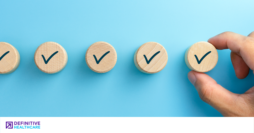 A hand places wooden pegs decorated with checkmarks in a horizontal row.