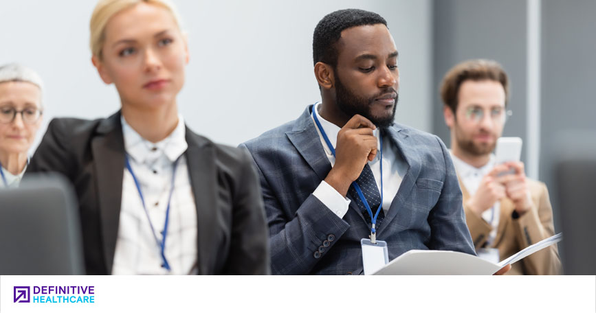 A diverse group of business people sit listening and reviewing materials