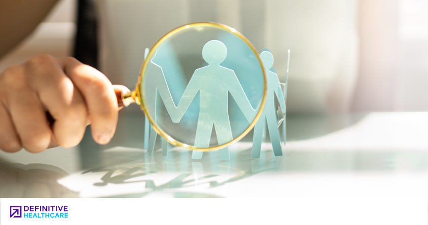A magnifying glass brings into focus a paper cutout shaped like people holding hands, symbolizing the work of healthcare staffing agencies.