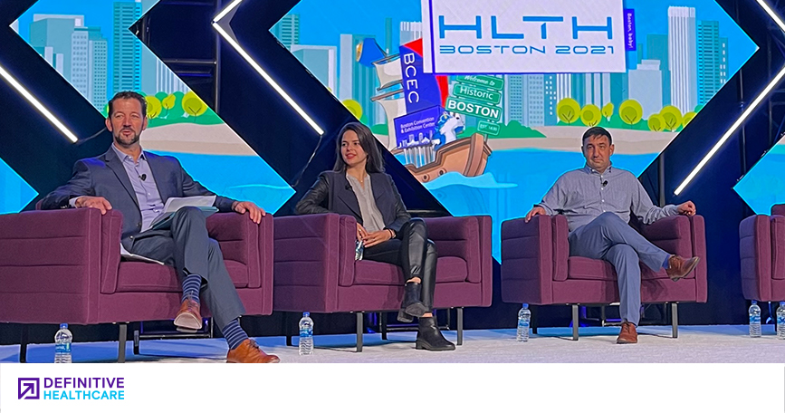 Three people, two men and one woman, sitting on stage in front of a background that says HLTH 2021