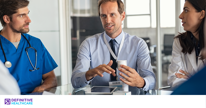 A medical administrator talks to a team of clinicians in a meeting room.