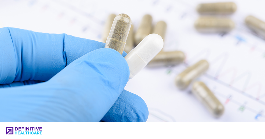 A hand in a blue latex glove holds up two pills.