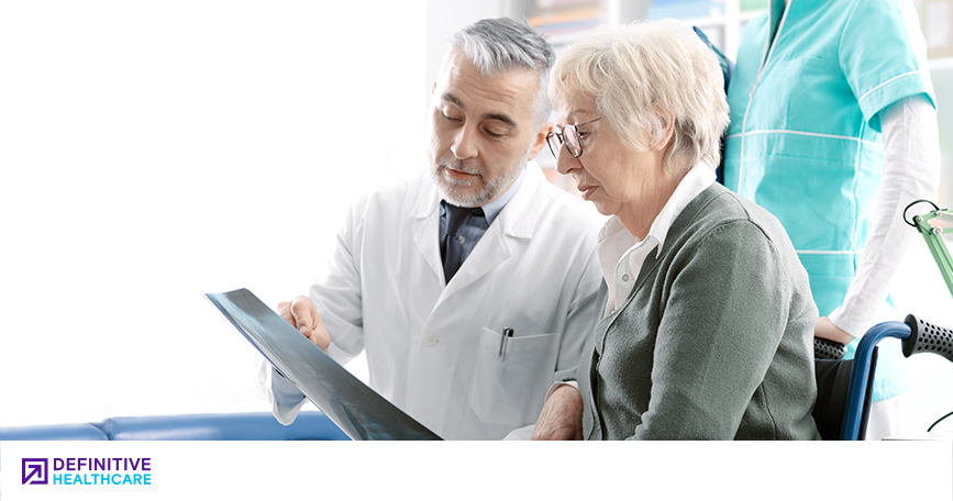 A male doctor showing an elderly woman in a wheelchair an X-ray with a person in a medical outfit standing behind them