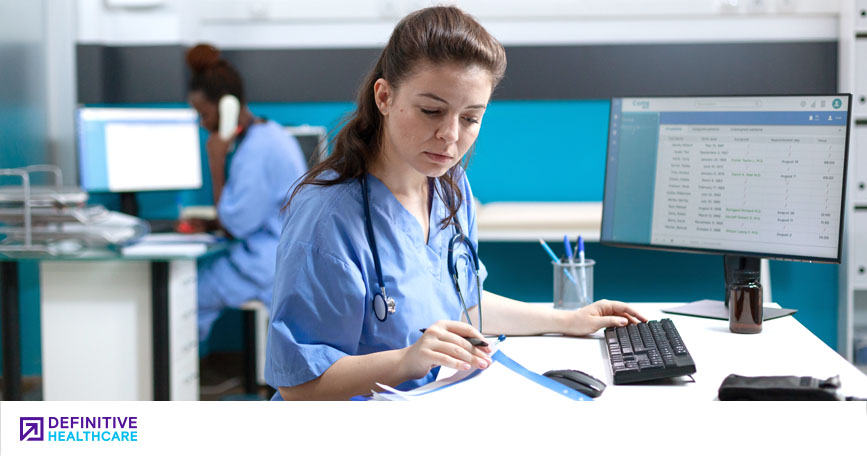 A healthcare worker sits at a computer and examines a chart.