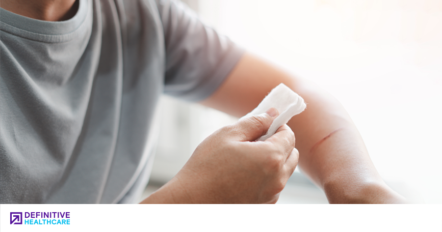 A white person in a gray t-shirt holding gauze up to a scratch on their arm