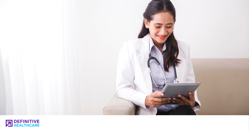 A doctor smiles while looking down at the tablet in her hands.