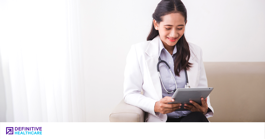 A doctor smiles while looking down at the tablet in her hands. 