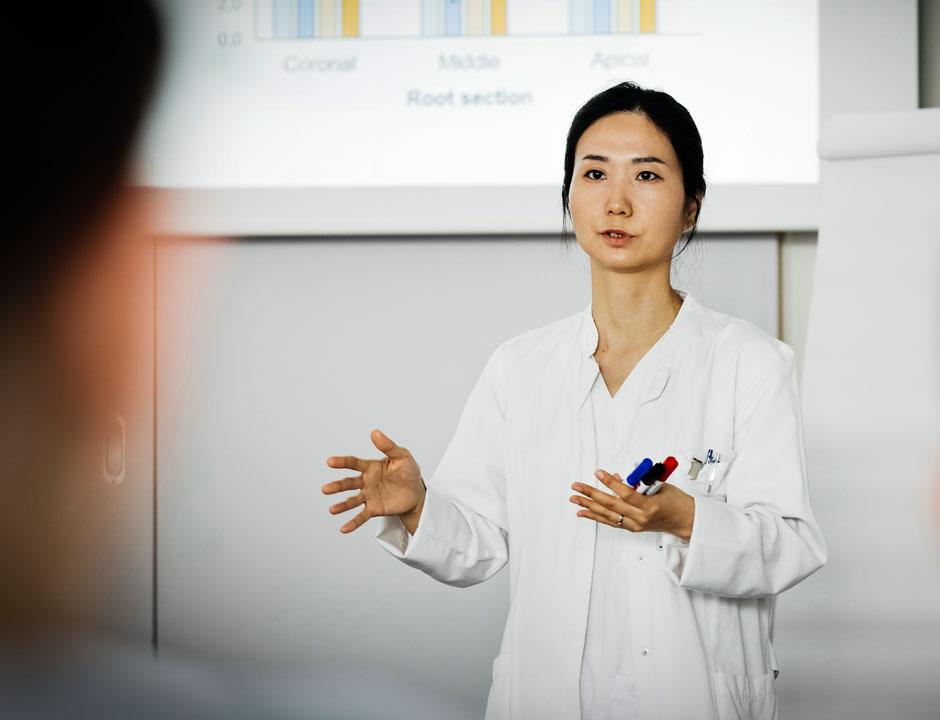A healthcare professional is standing up and giving a presentation. She is holding markers in her hand.