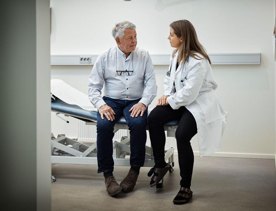 A female healthcare provider sits on an exam table next to a male patient.