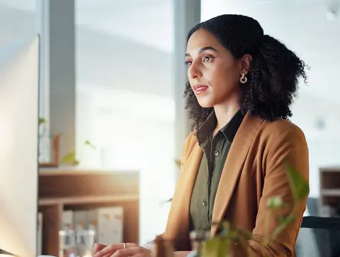 A woman in business attire looks at a computer screen.