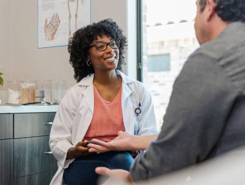 A female healthcare professional smiles while sitting down with a male patient.