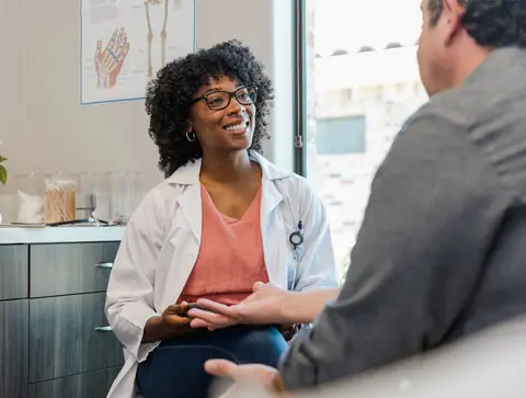 A female healthcare professional smiles while sitting down with a male patient.