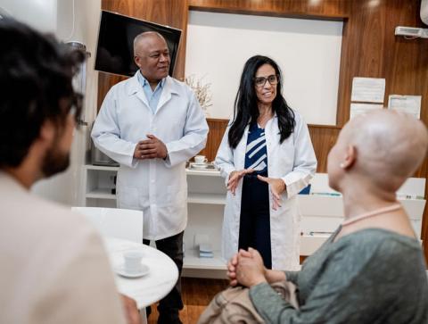 Two healthcare professionals in white coats stand in front of people sitting in a room.