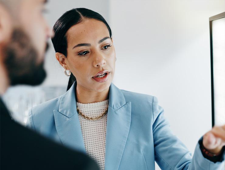 A woman in business casual attire is pointing at a screen